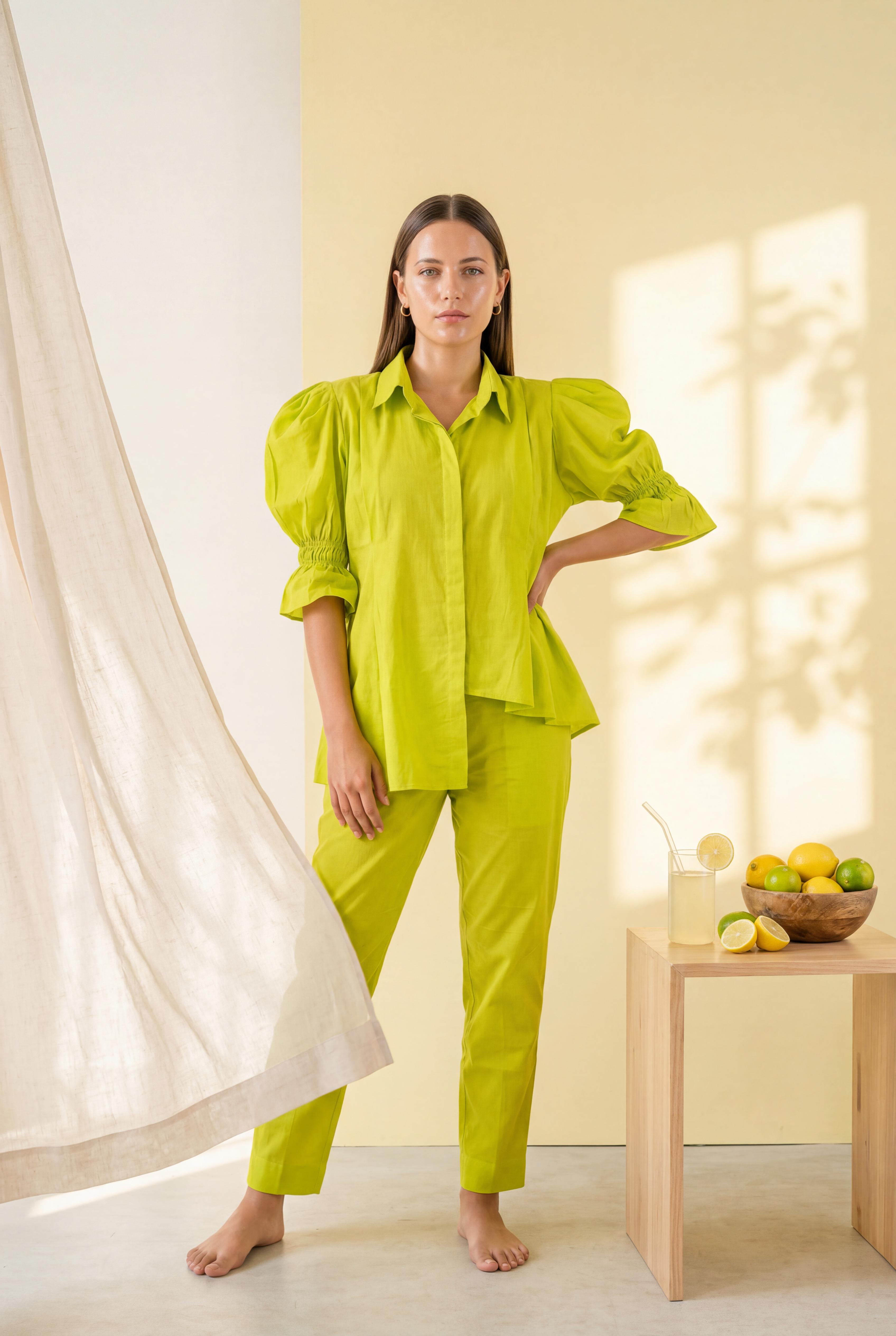 Woman wearing a bright green outfit standing in a softly lit room with a table and fruit.
